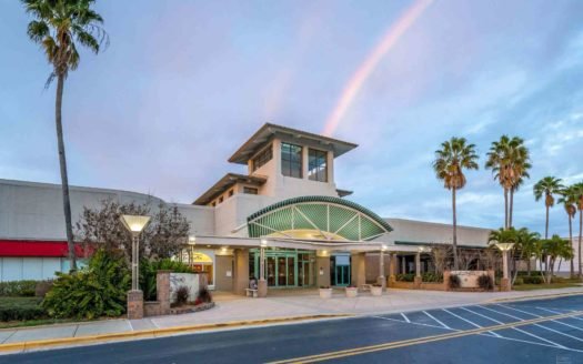 The Indian River Mall in Vero Beach, Florida at dusk with a rainbow in the sky with retail space available for lease.